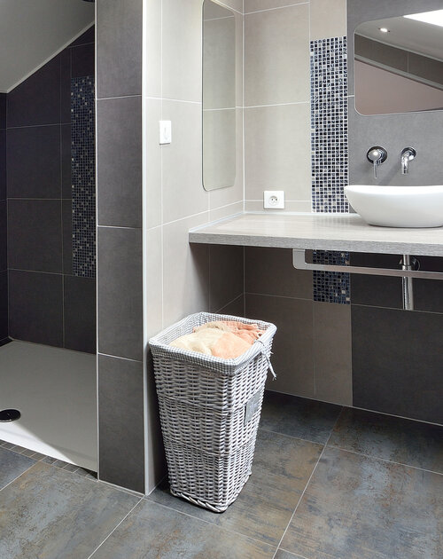 Suite parentale sous les combles avec mise en valeur des poutres. Création de rangements sous les rampants. Magnifique salle de douche épurée et raffinée. L'ensemble de l'espace est ouvert pour une très belle perspective. Les tons de dégradés de gris, bleu, chrome, sont réchauffés par le bois et les briques rouges.